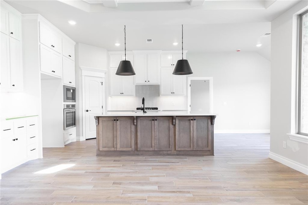 Kitchen with white cabinets, decorative light fixtures, a center island with sink, light wood-style flooring, and recessed lighting