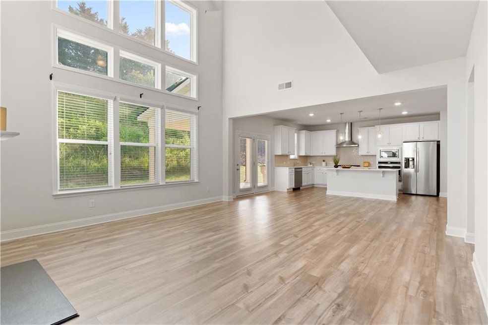 Unfurnished living room with light wood-style floors, healthy amount of natural light, a towering ceiling, baseboards, and recessed lighting