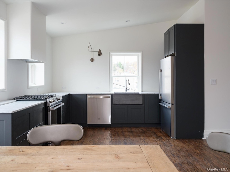 Kitchen with stainless steel appliances, dark wood-style floors, wall chimney range hood, light stone counters, and gray cabinets