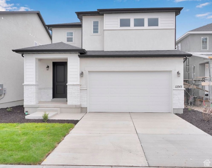 View of front of home with stone siding, an attached garage, driveway, and stucco siding