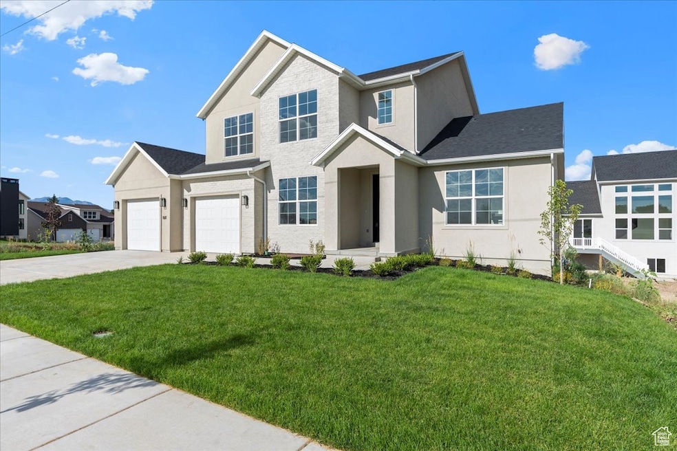 View of front of property with a garage, concrete driveway, a front lawn, and stucco siding and brick