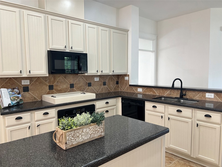 Craftman Style with Modern kitchen featuring light cabinetry, granite countertops, and a suite of black appliances with a tile backsplash. A central kitchen island provides additional workspace.