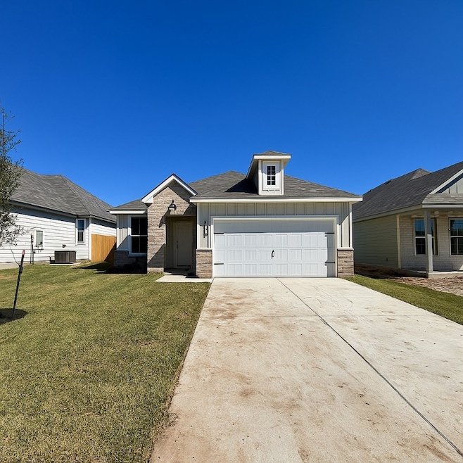 View of front of house featuring board and batten siding, driveway, a front yard, brick siding, and an attached garage