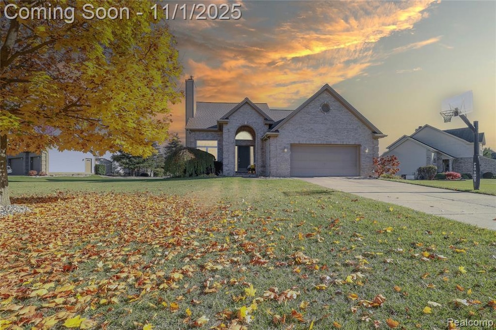 View of front of property with brick siding, a chimney, concrete driveway, and a yard