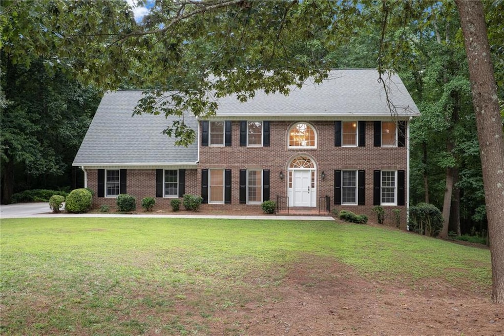 Colonial-style house featuring a front lawn, brick siding, and a shingled roof