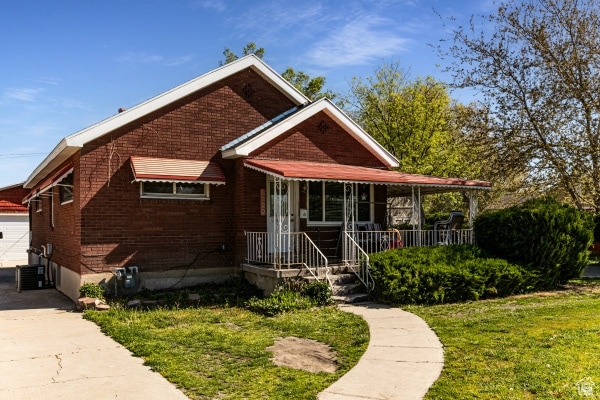 View of front of property featuring brick siding, a garage, covered porch, a front yard, and an outdoor structure