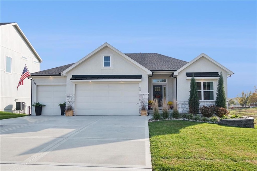 View of front of house with stone & stucco siding, a green yard, and concrete driveway.