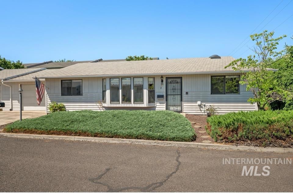 Single story home with a garage, a shingled roof, driveway, and a front lawn