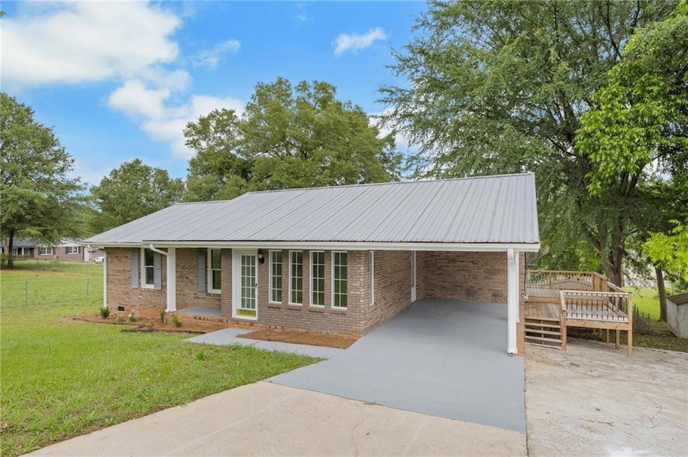 Ranch-style home featuring driveway, brick siding, a carport, and a deck