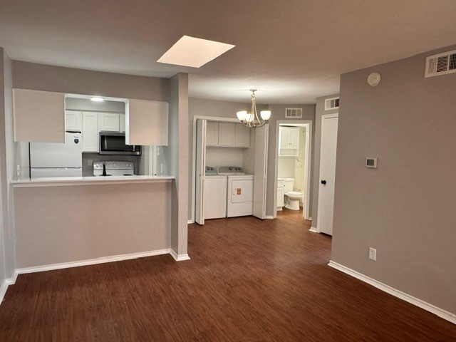 Kitchen featuring white appliances, white cabinets, dark wood finished floors, a chandelier, and light countertops