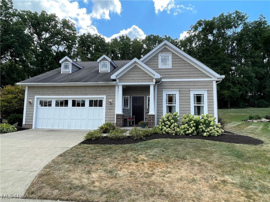 Craftsman-style home featuring a garage, a front lawn, driveway, and view of wooded area