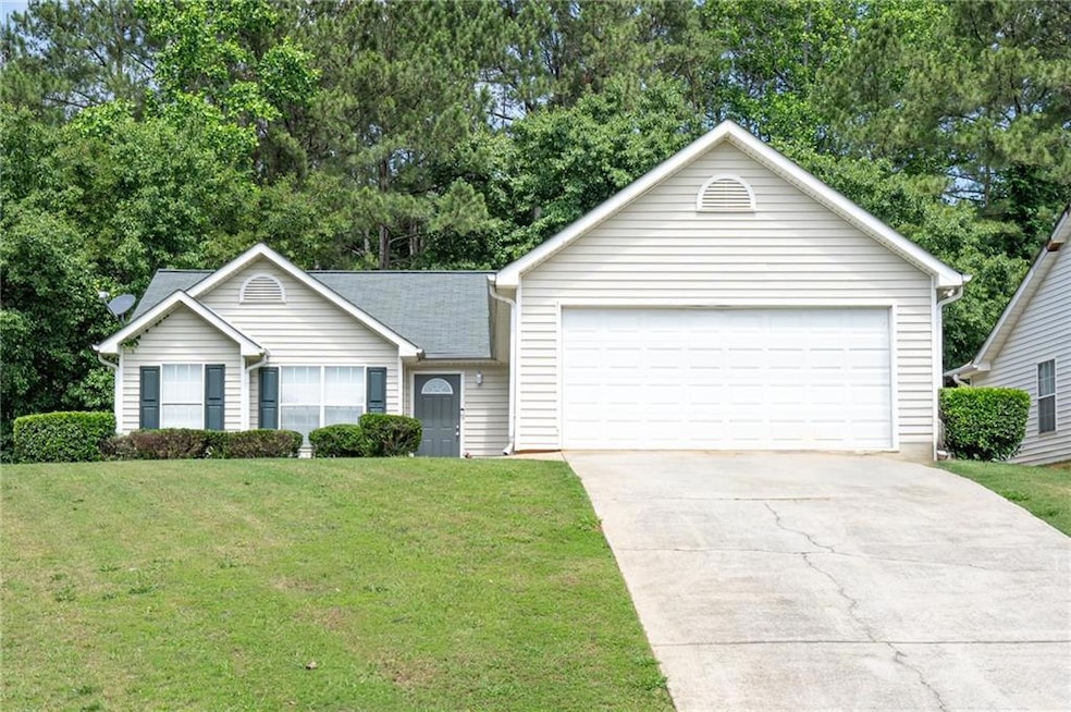Single story home with a front yard, view of wooded area, and concrete driveway