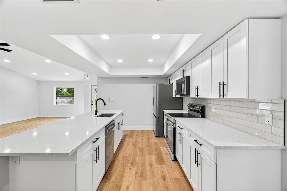 Kitchen with light wood-style floors, white cabinetry, stainless steel appliances, recessed lighting, and light stone countertops