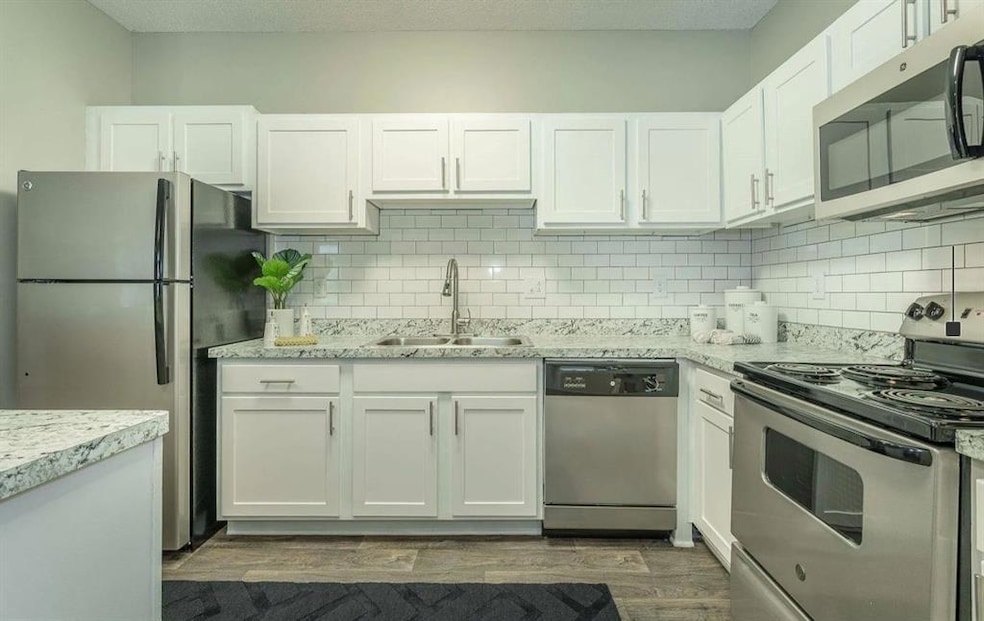 Kitchen with appliances with stainless steel finishes, white cabinetry, dark wood-style flooring, tasteful backsplash, and light stone countertops