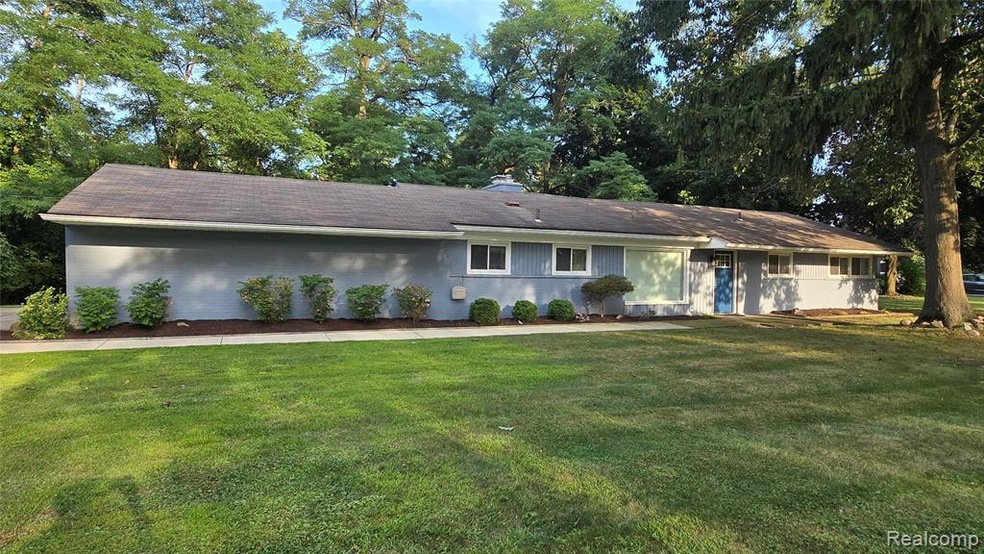 Ranch-style home featuring a front yard, view of scattered trees, and a chimney