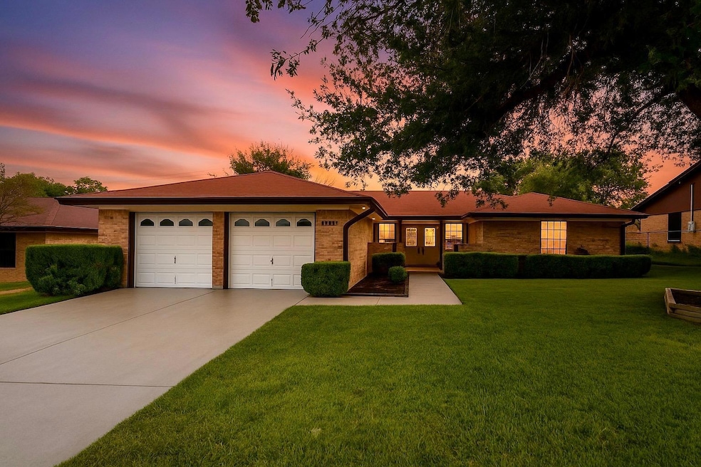 Ranch-style house with a yard, driveway, brick siding, and an attached garage