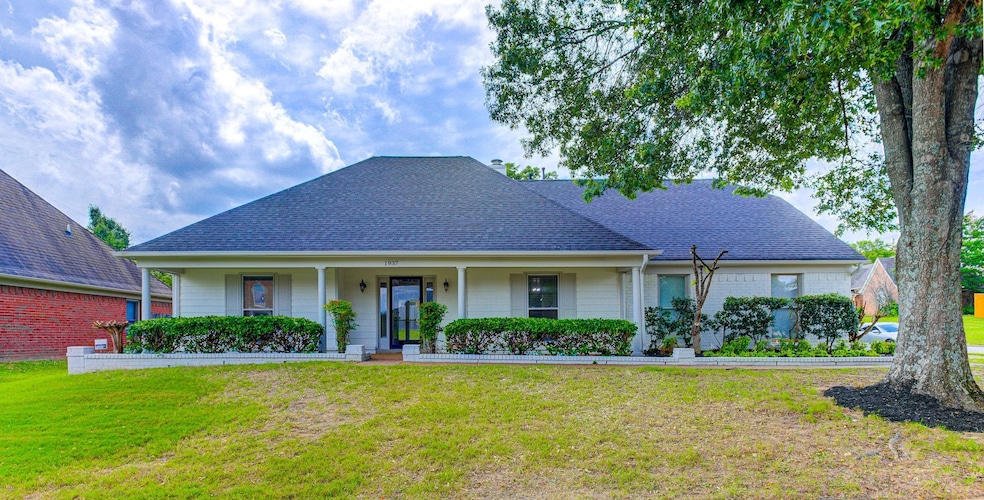 View of front facade with a front yard, a shingled roof, a porch, and brick siding