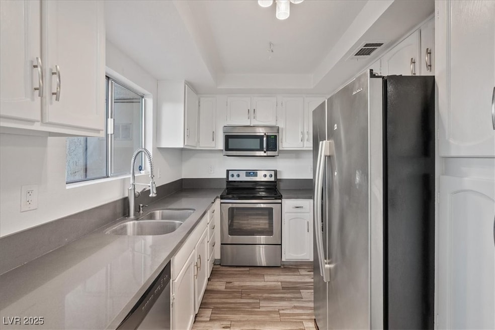 Kitchen with stainless steel appliances, white cabinets, a tray ceiling, light wood-style floors, and dark stone countertops
