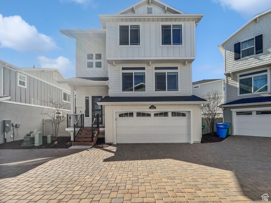View of front facade featuring board and batten siding, decorative driveway, a garage, and central air condition unit