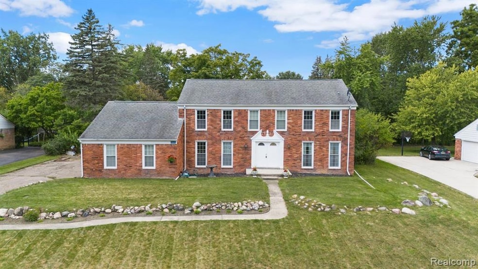 Colonial house featuring a front yard, brick siding, a shingled roof, and driveway