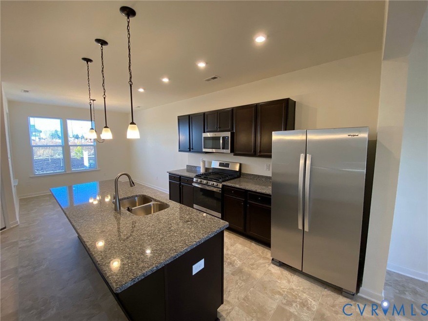 Kitchen with stainless steel appliances, dark stone countertops, pendant lighting, a center island with sink, and recessed lighting