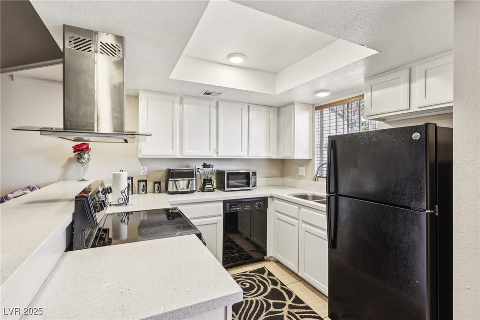 Kitchen with island range hood, a raised ceiling, white cabinets, a sink, and black appliances