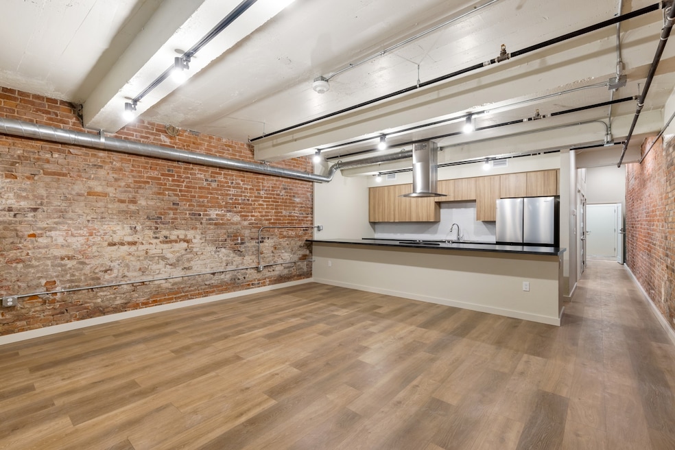 Kitchen with sink, stainless steel refrigerator, wood-type flooring, brick wall, and kitchen peninsula
