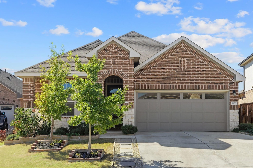 View of front of home with brick siding, driveway, an attached garage, roof with shingles, and stone siding