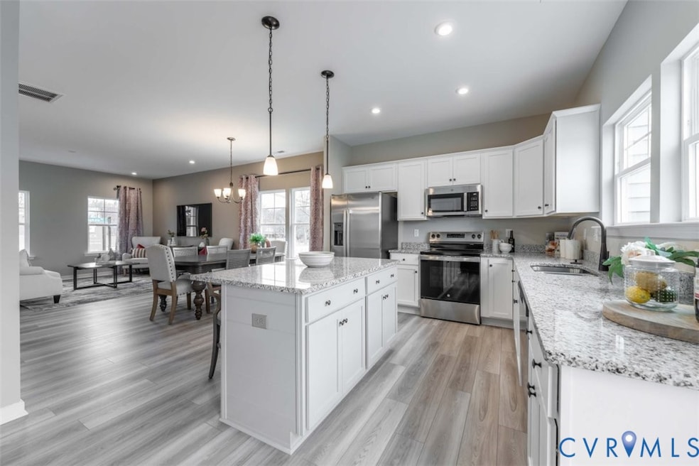Kitchen with stainless steel appliances, white cabinetry, a kitchen island, open floor plan, and light stone counters