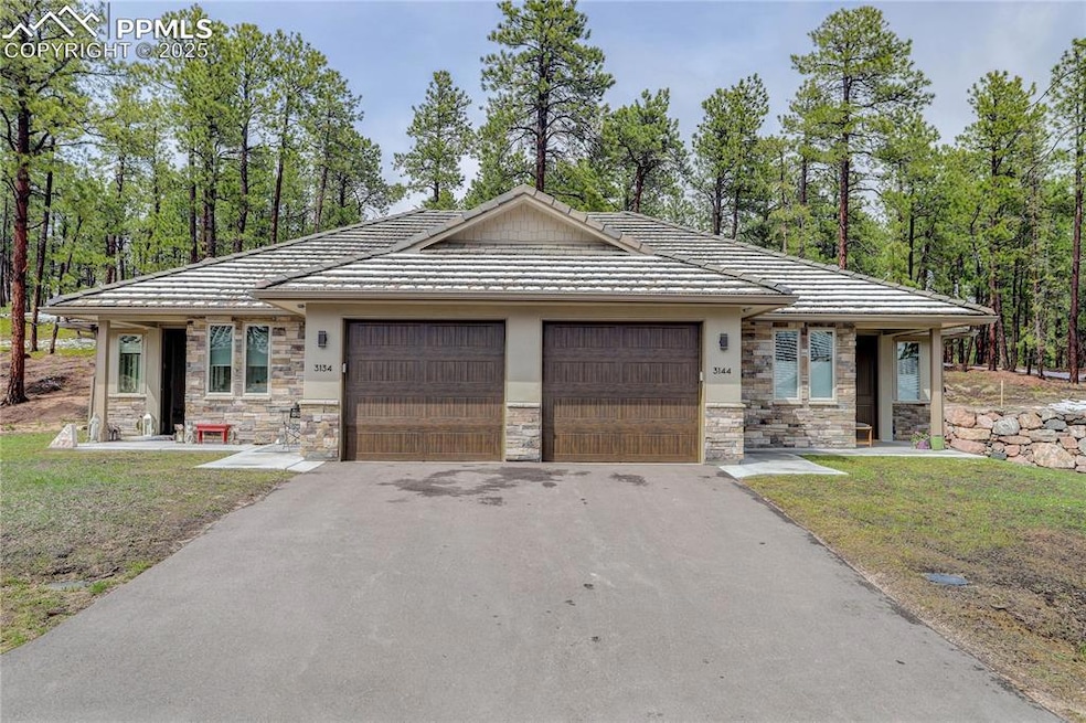 View of front of property featuring an attached garage, stone siding, a tile roof, and asphalt driveway