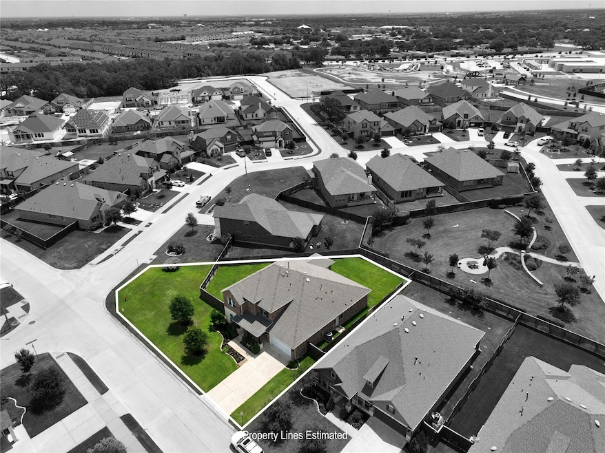 This aerial photo showcases a spacious, corner-lot home with a large, well-maintained yard in a suburban neighborhood. The property is bordered by streets on two sides and features a fenced backyard, offering privacy and ample outdoor space. The surrounding area is residential with similar homes, providing a community feel.