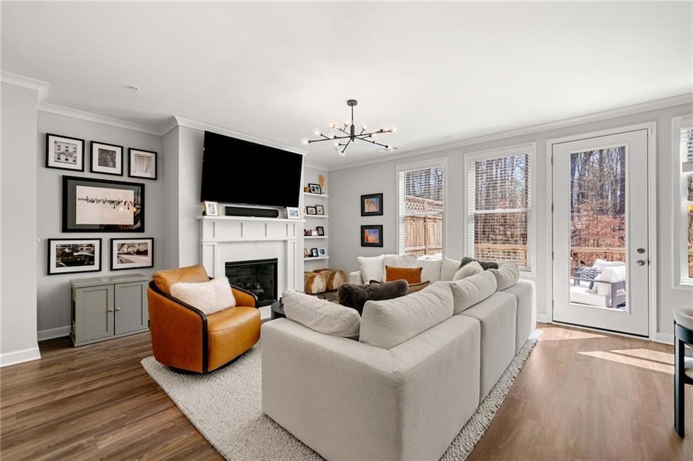 Living room with a chandelier, crown molding, built in shelves, wood finished floors, and a glass covered fireplace