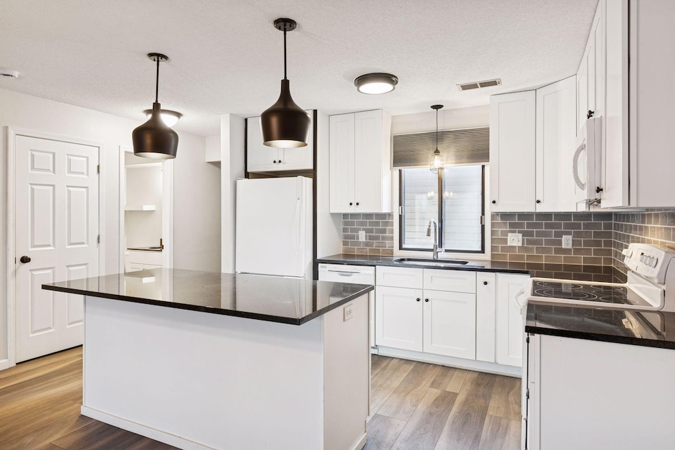 Gorgeous updated kitchen featuring granite countertops, tall cabinetry, stylish tile backsplash, and modern lighting.