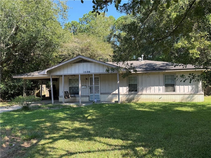 View of front of home featuring a porch, board and batten siding, a front lawn, a carport, and brick siding