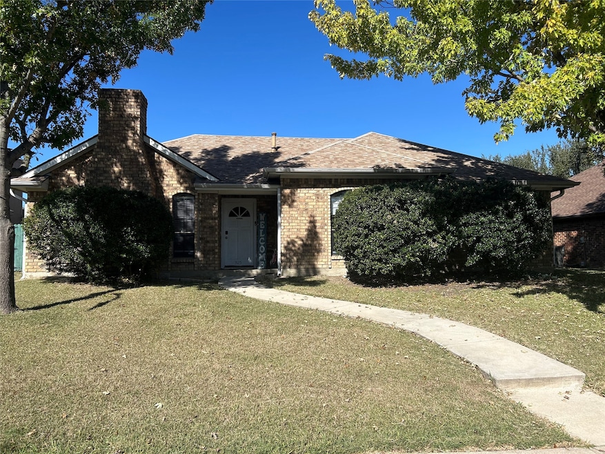 View of front facade featuring a front yard, brick siding, a chimney, and a shingled roof