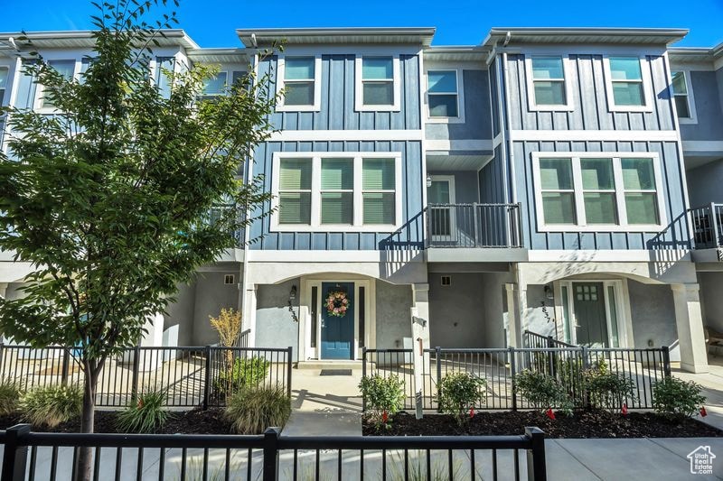 View of front of property with board and batten siding, stucco siding, a fenced front yard, and a balcony