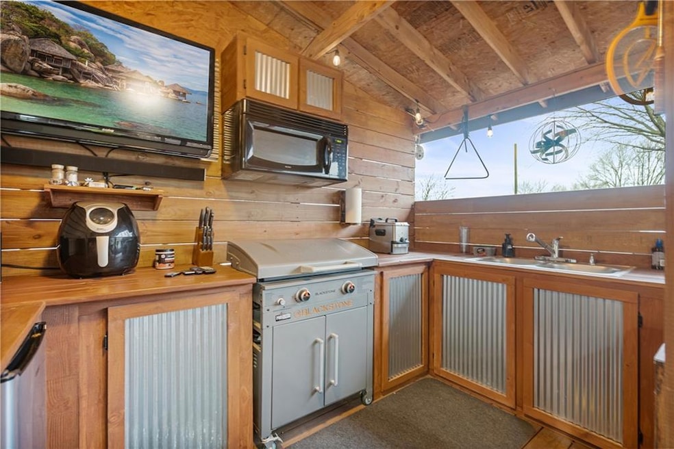 Kitchen featuring black microwave, lofted ceiling, wooden walls, a sink, and light countertops