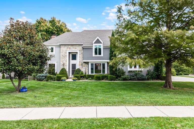 View of front of house with stone siding, a front lawn, stucco siding, and a chimney