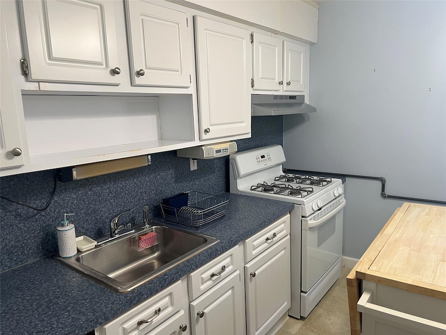 Kitchen with tasteful backsplash, a sink, white cabinets, under cabinet range hood, and white range with gas stovetop