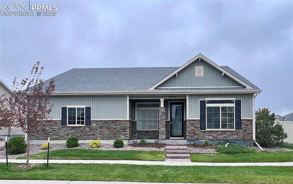 Craftsman house featuring stone siding, a front yard, a shingled roof, and a porch