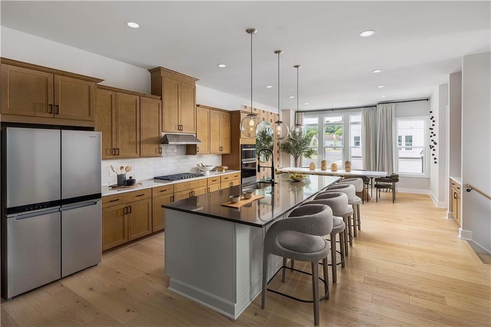 Kitchen with a breakfast bar, a kitchen island with sink, light hardwood / wood-style flooring, pendant lighting, and stainless steel appliances