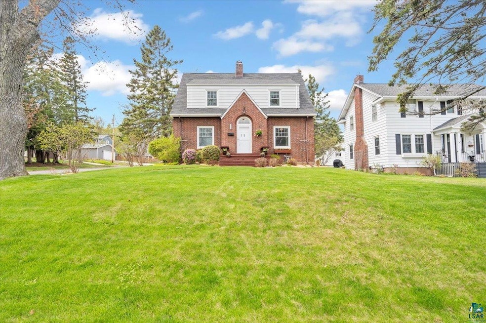 Dutch colonial featuring brick siding, a chimney, and a front lawn