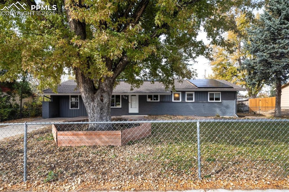 Ranch-style home with brick siding, a fenced front yard, solar panels, and roof with shingles