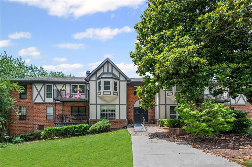 English style home with a front yard, brick siding, stucco siding, and a balcony