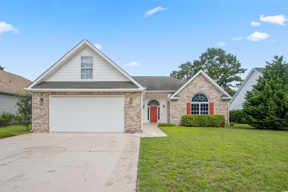 Traditional-style home featuring a front lawn, concrete driveway, a garage, brick siding, and roof with shingles