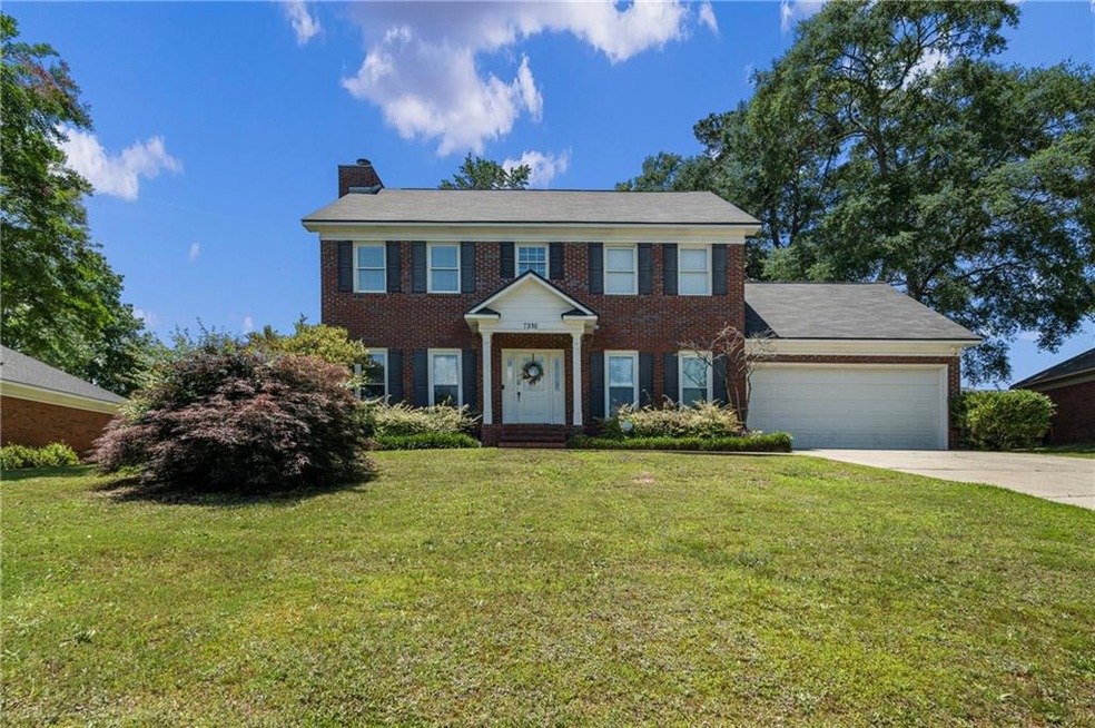 View of front of property featuring driveway, a chimney, brick siding, an attached garage, and a front lawn