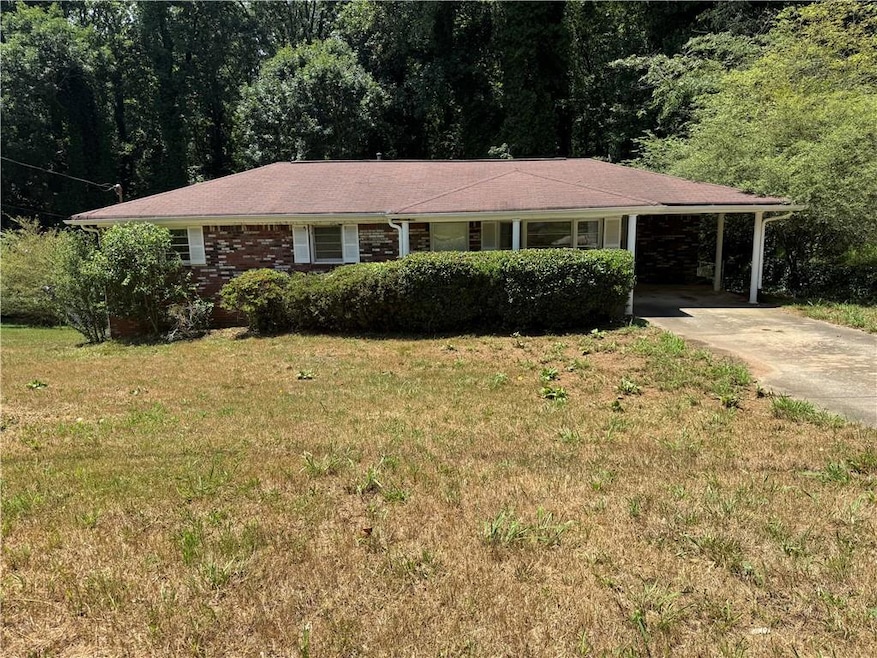 Single story home featuring an attached carport, concrete driveway, a front yard, and brick siding