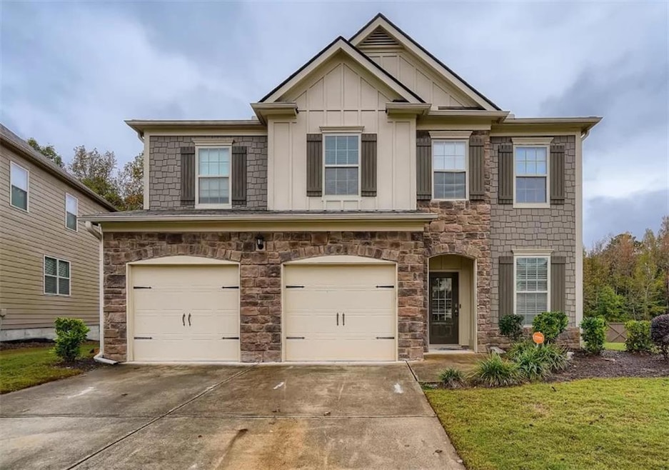 View of front of home with board and batten siding, a garage, concrete driveway, stone siding, and a front lawn
