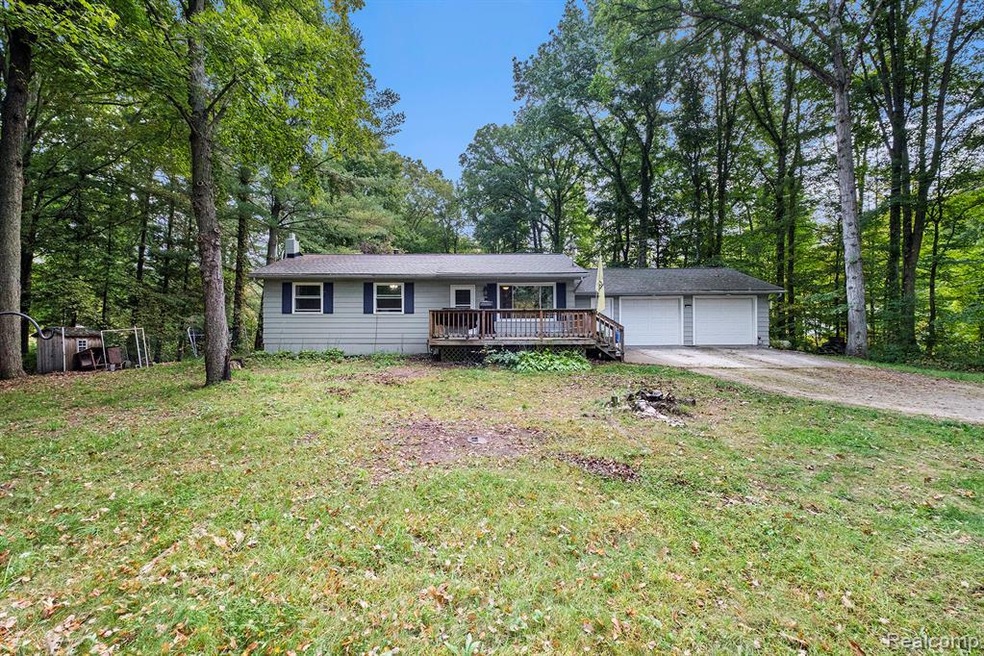 Single story home featuring a front lawn, driveway, a wooden deck, and view of scattered trees