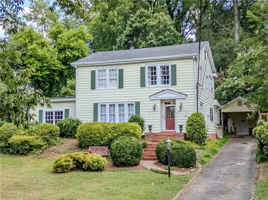 Colonial home with a front lawn, view of wooded area, and driveway